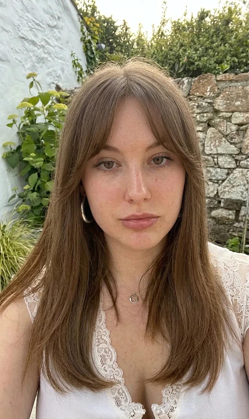 After the bangs simulation: the same woman, same garden and lighting, rendered with soft curtain bangs framing her face