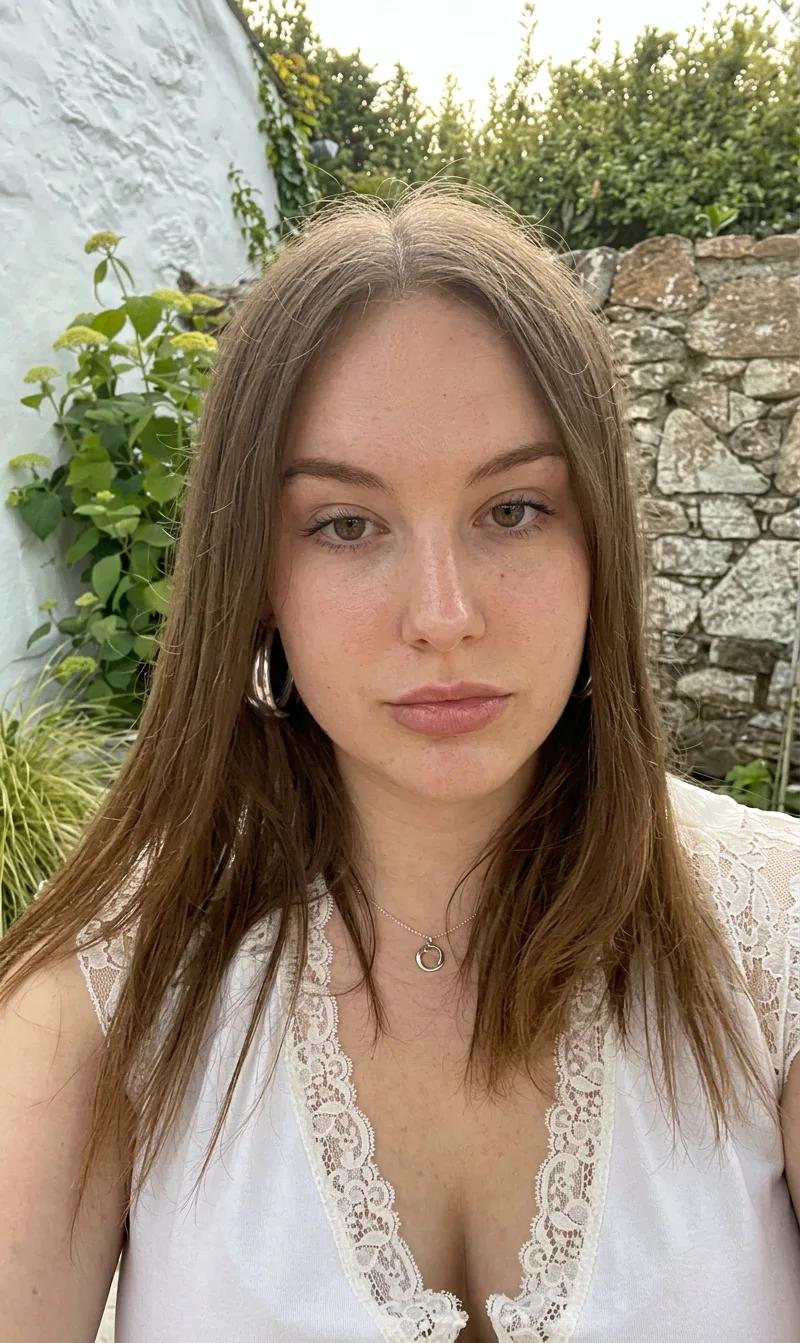 Before the bangs simulation: woman with a center part and no bangs, full forehead visible, in an outdoor selfie