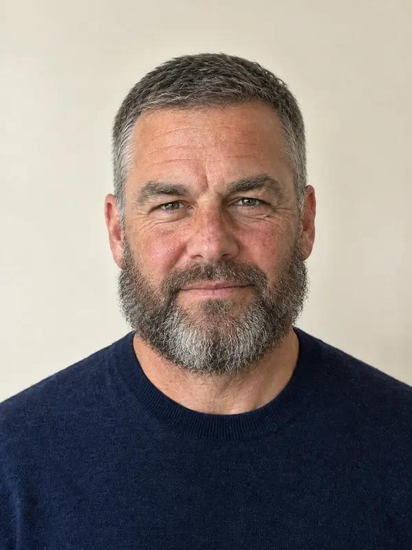 A man in his forties with a flat short cut and a full beard wide at the cheeks