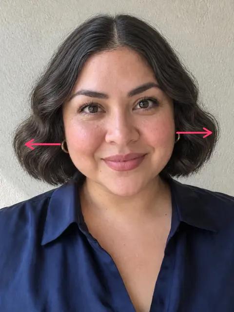 A woman in her late thirties with a round face and a chin-length cut with wide waves, arrows pointing out to the width at her cheeks
