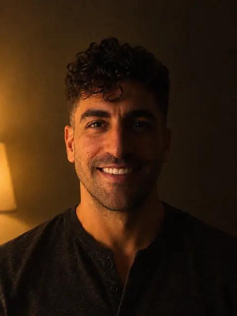 The same man in a dim room under a warm lamp, half his face in shadow